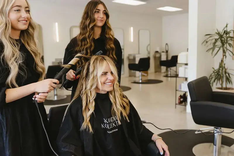 Two stylists finish a guest's long, styled blonde extensions in the salon