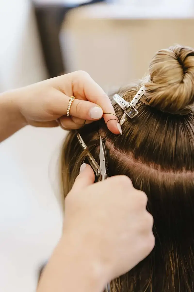 A stylist places small beads along a parted section of hair to build an NBR beaded row